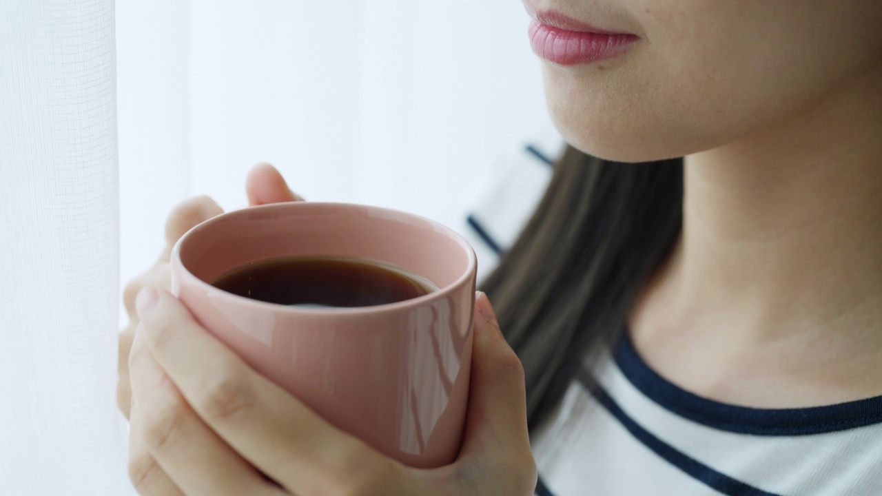 4K年轻的亚洲女子在公寓客厅里喝着热咖啡。视频素材