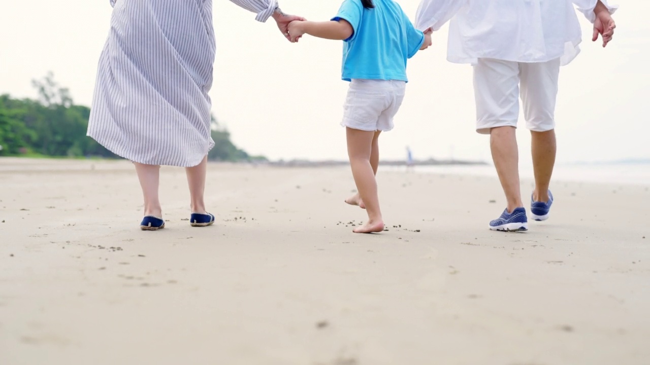 在阳光明媚的日子里，4K亚洲祖父母带着孙儿女孩一起走在海滩上视频素材