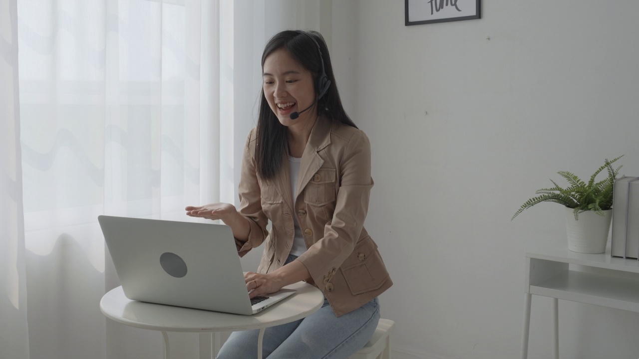 年轻的亚洲女商人戴着耳机视频电话和解释会议在线在家，女性戴着耳机会议和谈话的工作，业务和沟通的概念。视频素材