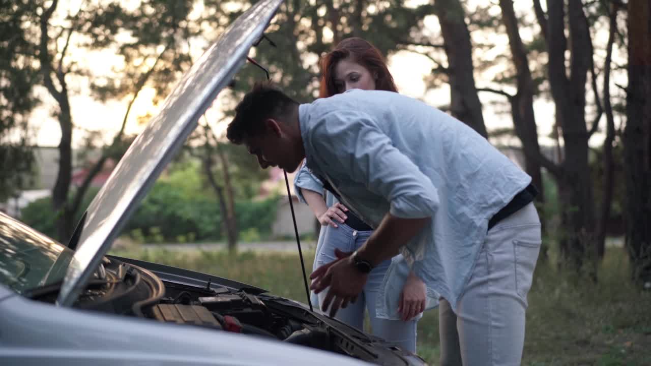 侧视图肖像集中的男子倾斜在开放的汽车引擎盖与妇女站在背景。忧心忡忡的白人男女在郊区开车时出了故障。视频素材