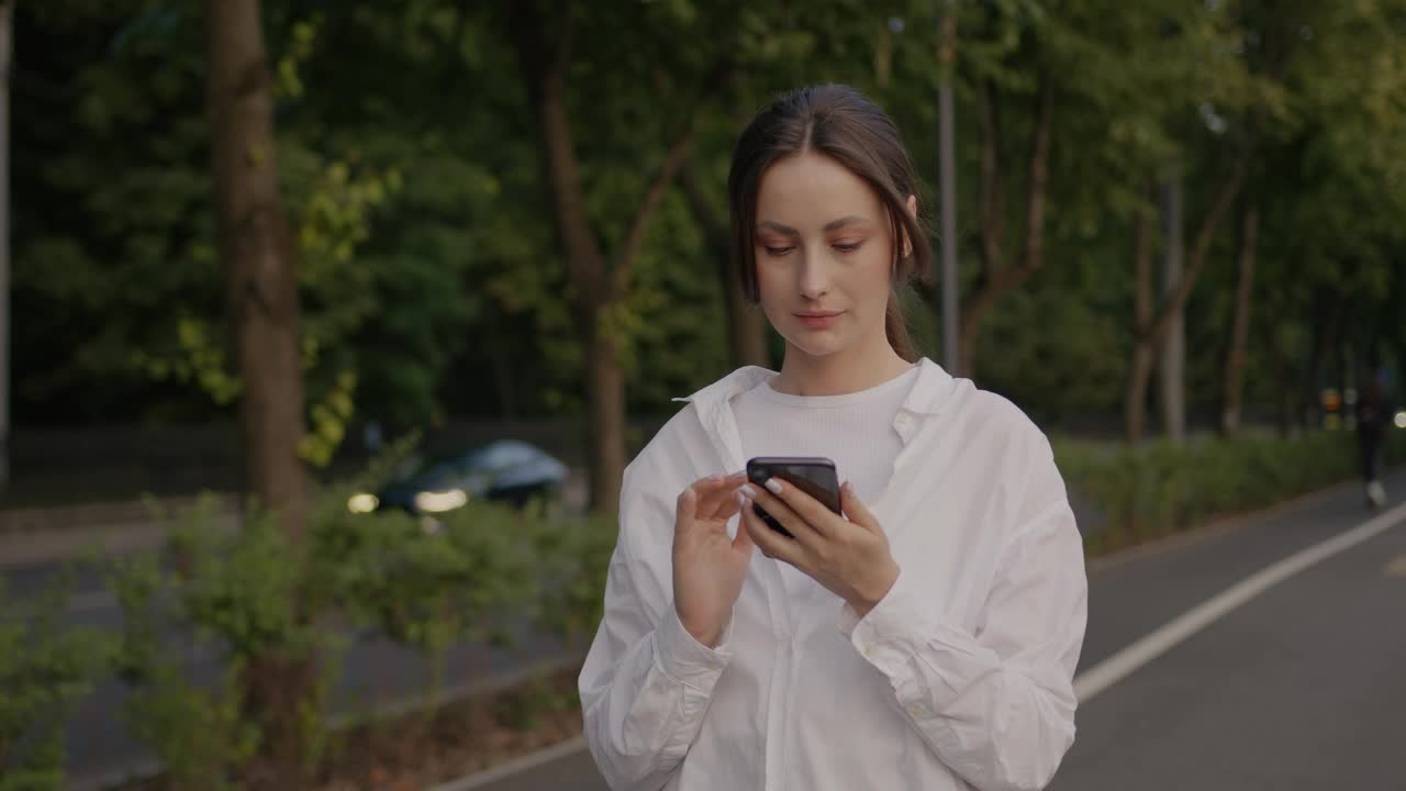 女人在街上一边用手机聊天一边发短信，面带微笑视频素材