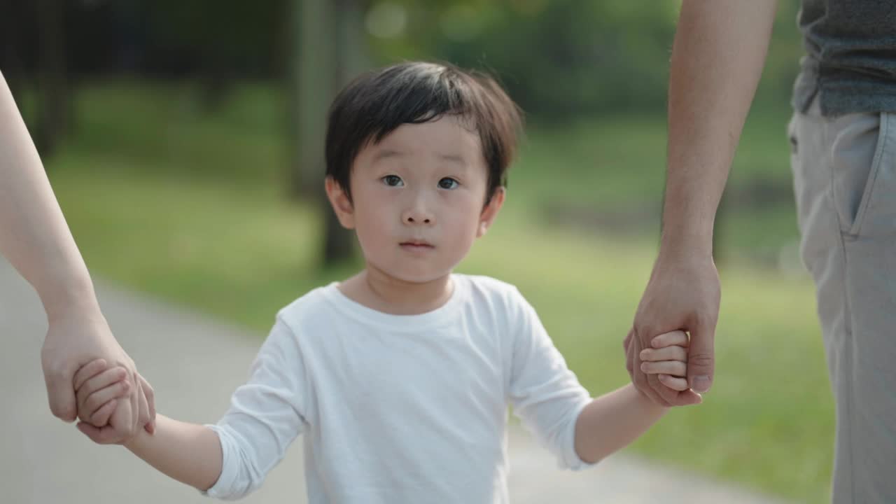 亚洲华人男孩牵着父母的手在公园散步视频素材