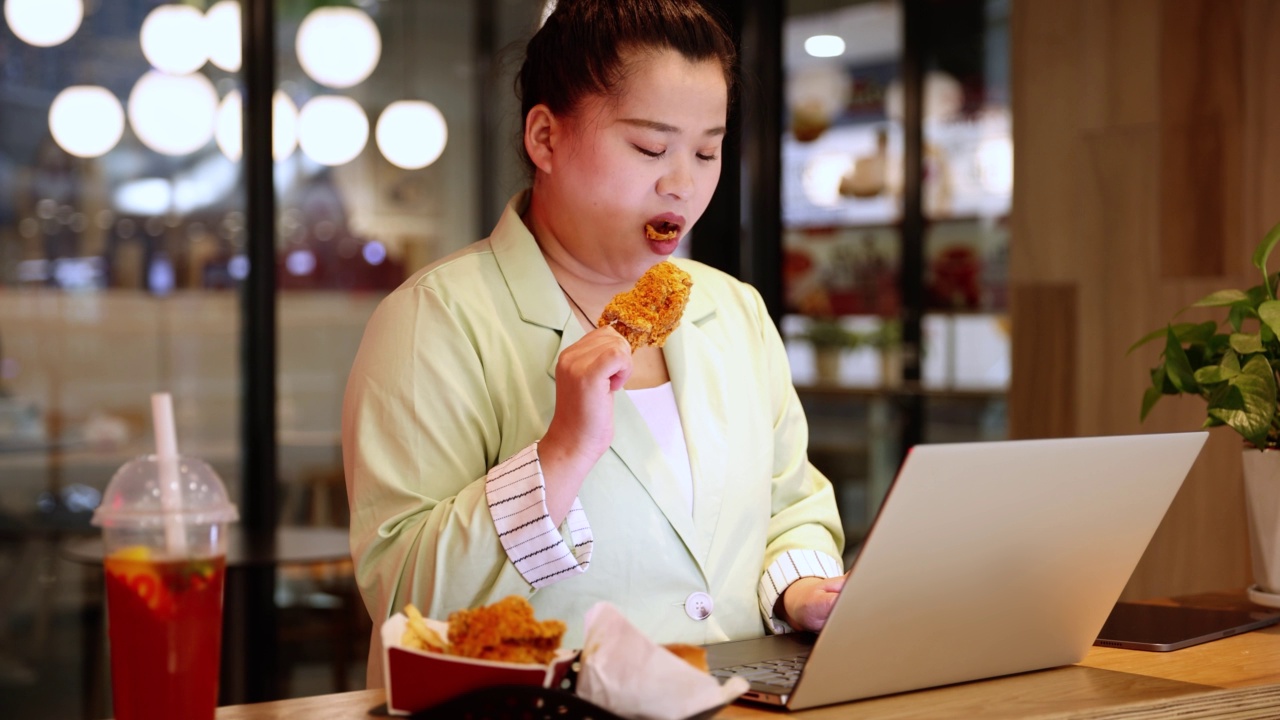 女商人一边用笔记本电脑工作一边吃炸鸡视频素材