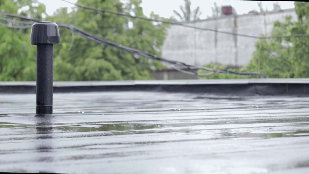 雨点敲打着屋顶，大雨滂沱。这座建筑的平屋顶覆盖着防水材料，可以防雨。橡胶、卷材屋面及防水材料。视频素材