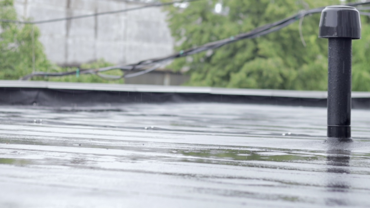 雨点敲打着屋顶，大雨滂沱。这座建筑的平屋顶覆盖着防水材料，可以防雨。橡胶、卷材屋面及防水材料。视频素材