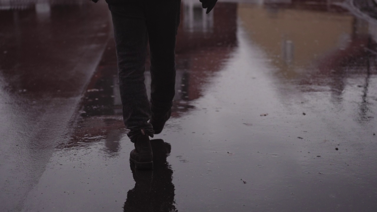 穿着皮鞋的男人在雨中走在潮湿的柏油路上视频素材