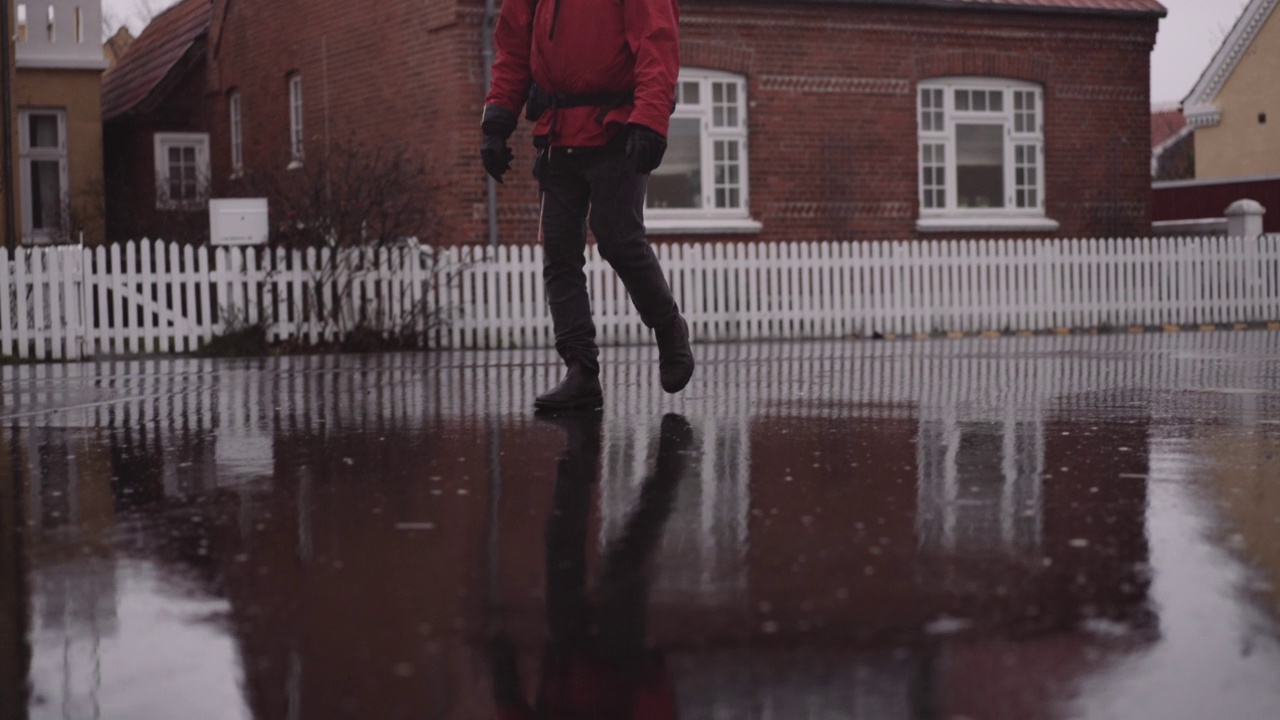 穿着冬装的背包男子在雨中走在潮湿的柏油路上视频素材