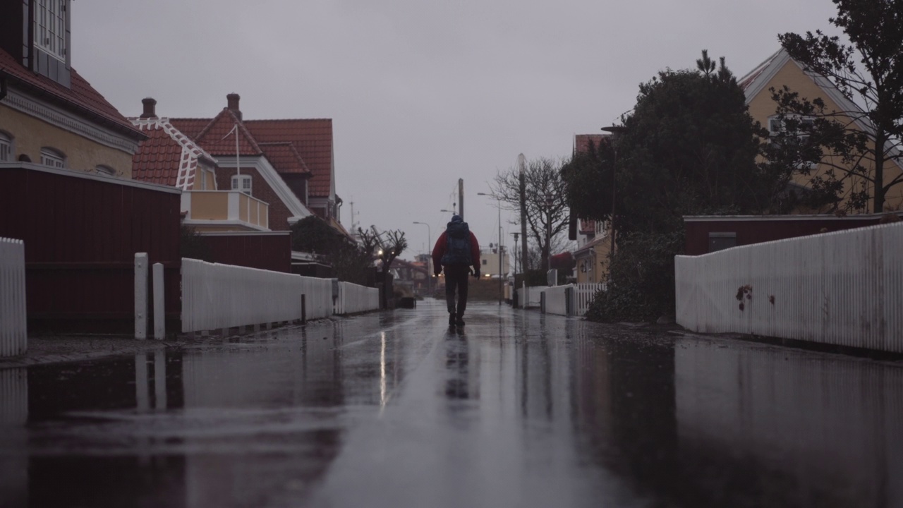 雨中背着背包的男子走在住宅之间的湿路上视频素材