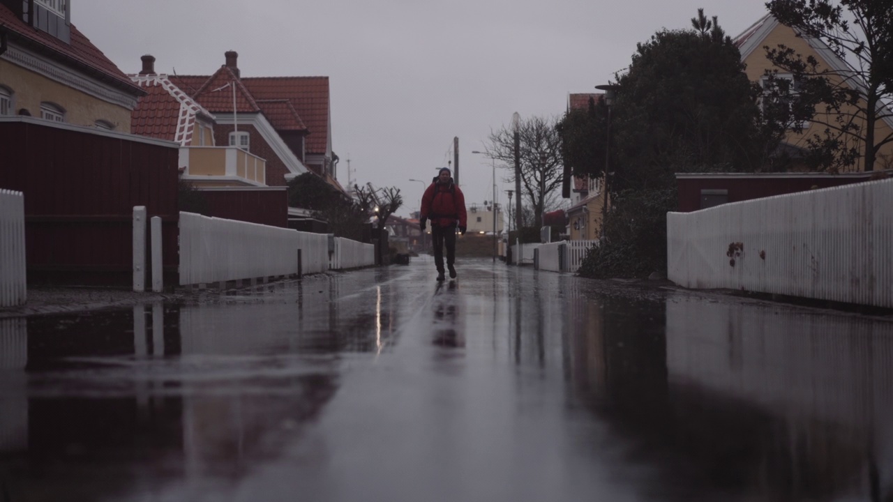 雨中背着背包的男子走在住宅之间的湿路上视频素材