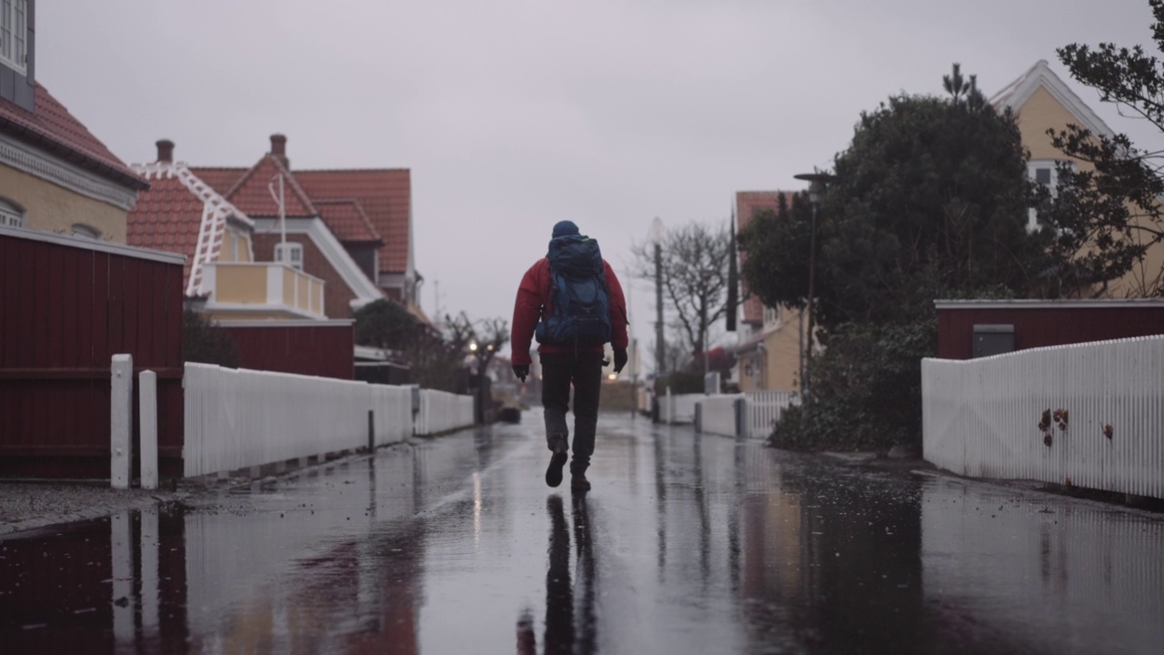 穿着冬装的背包男子在雨中走在潮湿的柏油路上视频素材