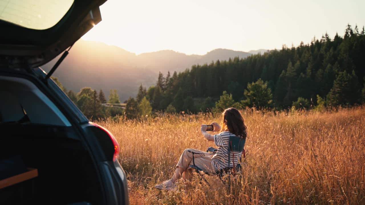 一名年轻女子在独自驾车旅行时用智能手机拍照视频素材