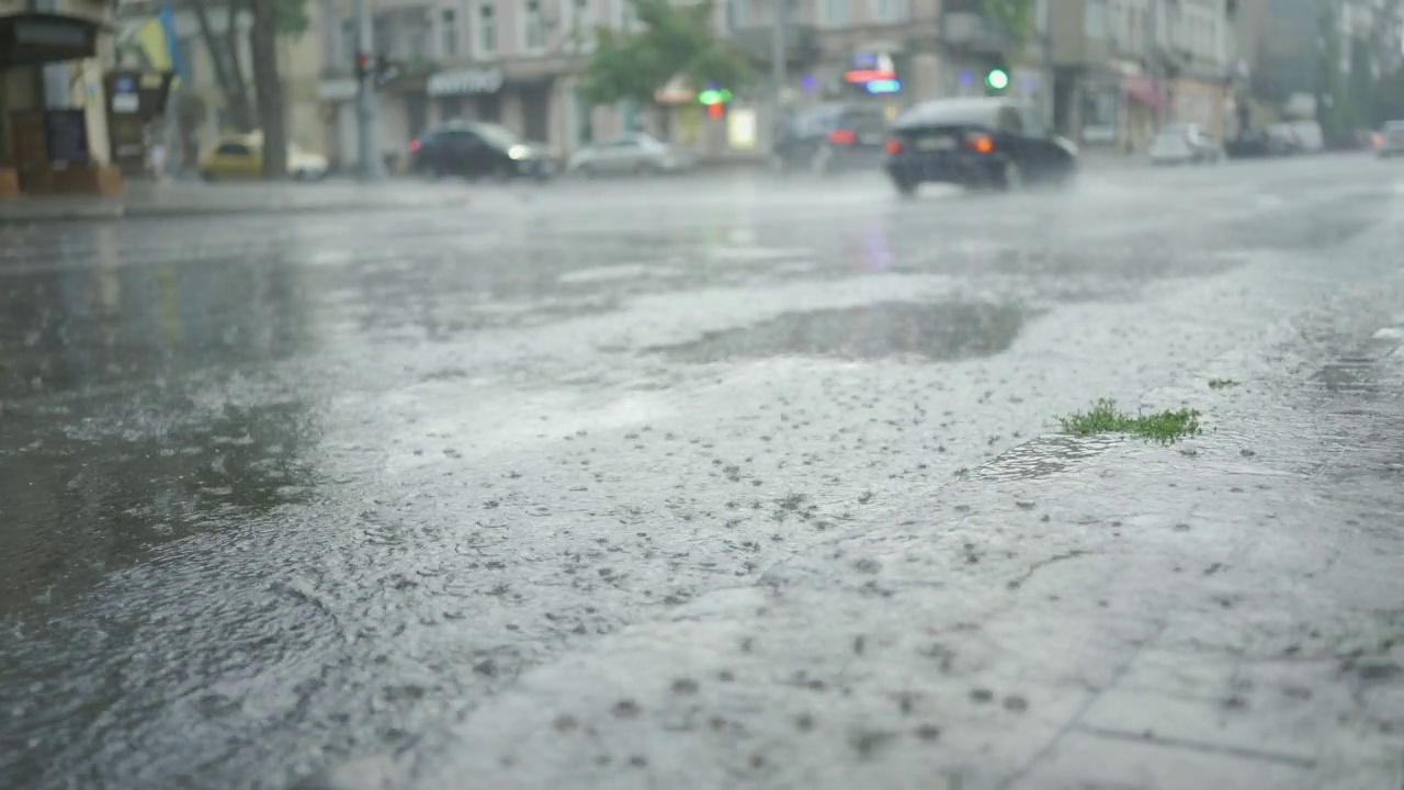 雨滴落在路上，背景是汽车行驶。城里下起了暴雨。视频素材