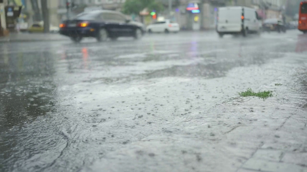 雨滴落在路上，背景是汽车行驶。城里下起了暴雨。视频素材