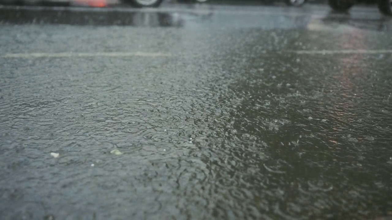 雨滴落在路上的特写，背景是汽车行驶。城里下起了暴雨。视频素材