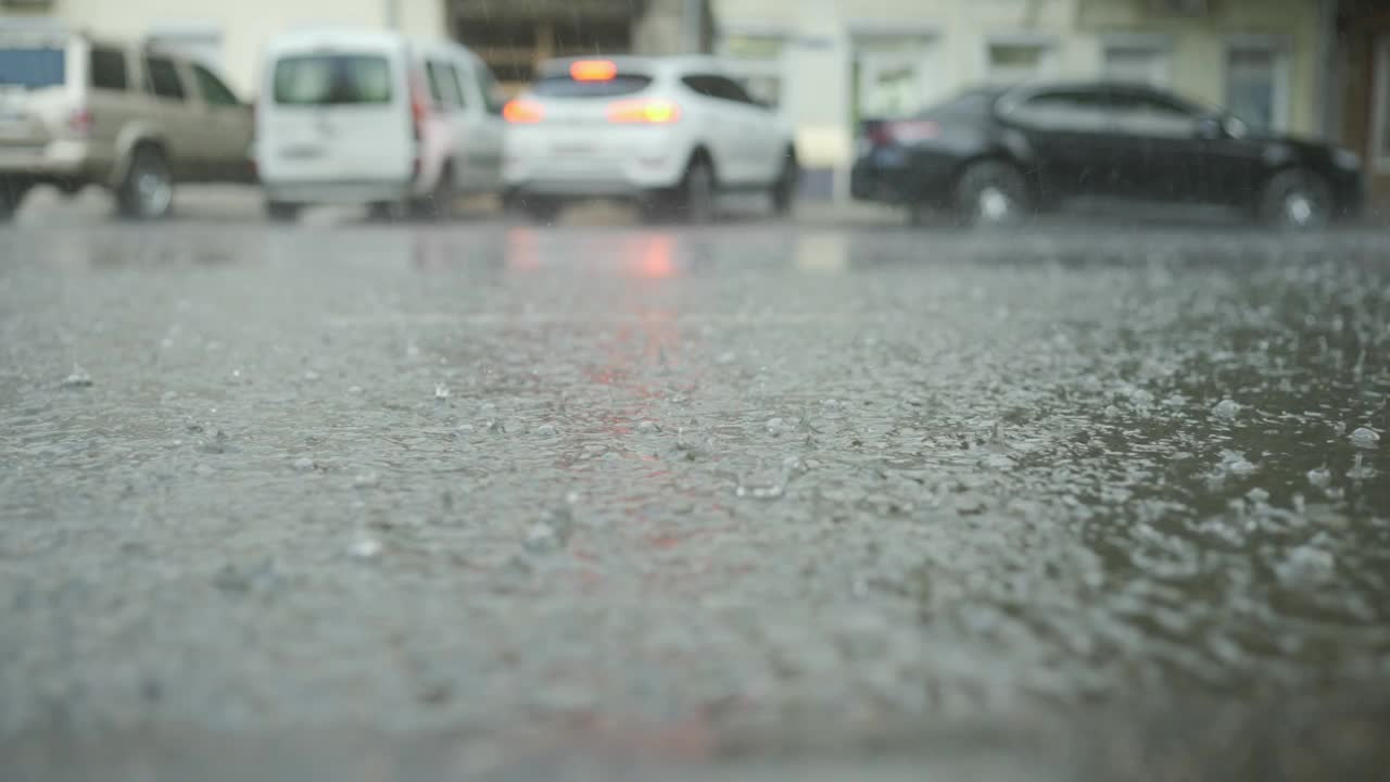 慢动作，雨滴落在路上，背景是汽车。城里下起了暴雨。视频素材