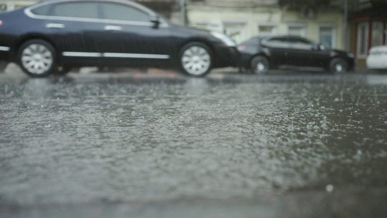 雨滴落在路上的特写，背景是汽车行驶。城里下起了暴雨。视频素材