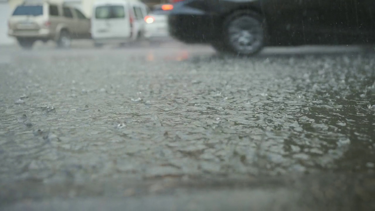 雨滴落在路上的特写，背景是汽车行驶。城里下起了倾盆大雨。视频素材