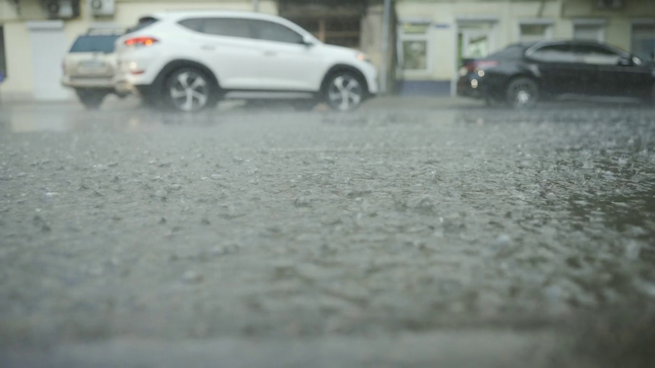 雨滴落在路上的特写，背景是汽车行驶。城里下起了暴雨。视频素材