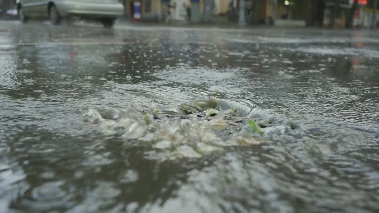 一股雨水流进排水沟，背景是正在行驶的汽车。城里下起了暴雨。视频素材