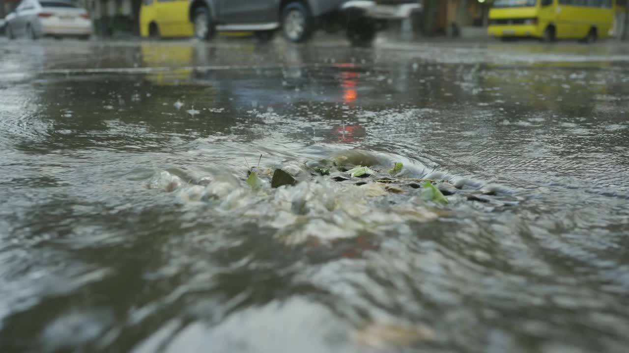 一股雨水流进排水沟，背景是正在行驶的汽车。城里下起了暴雨。视频素材