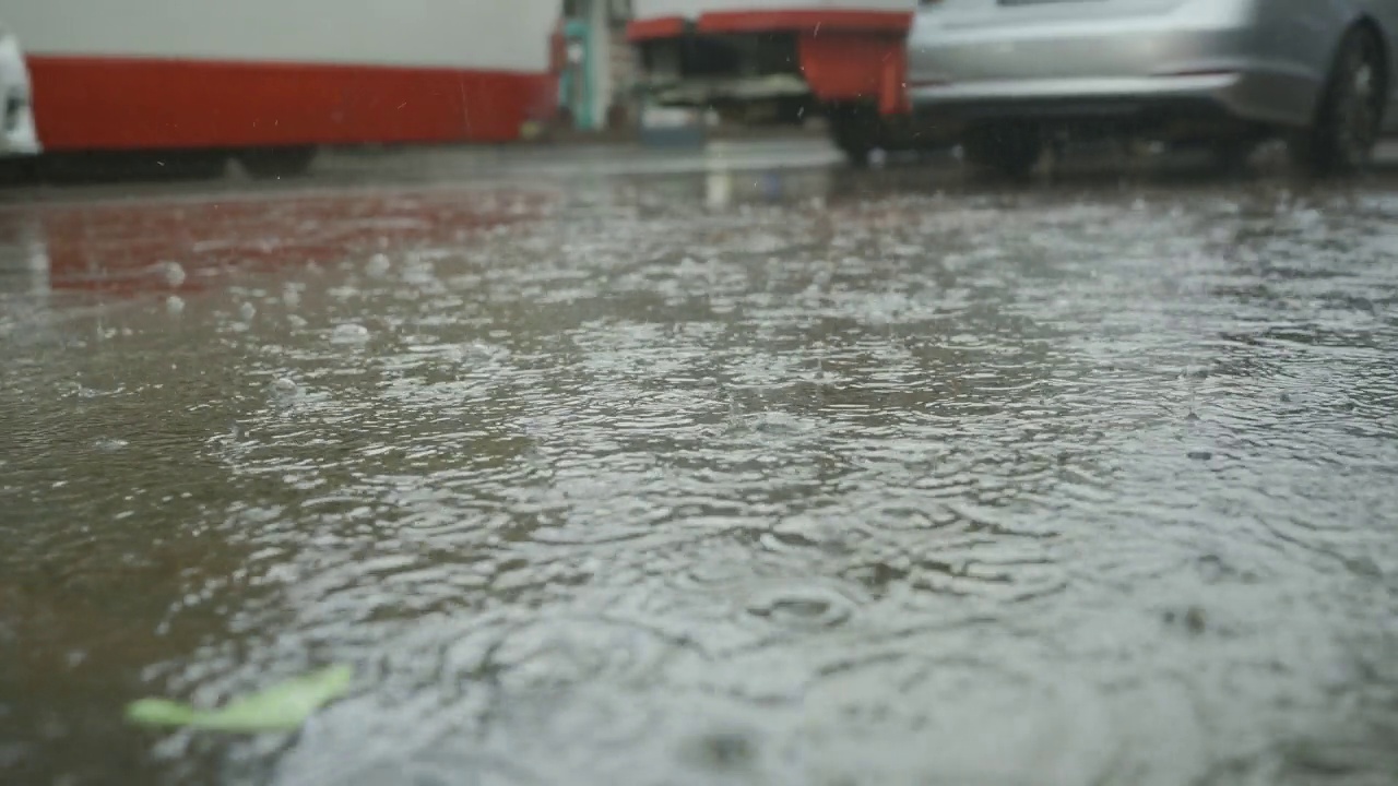 雨滴落在路上，背景是汽车行驶。城里下起了暴雨。视频素材