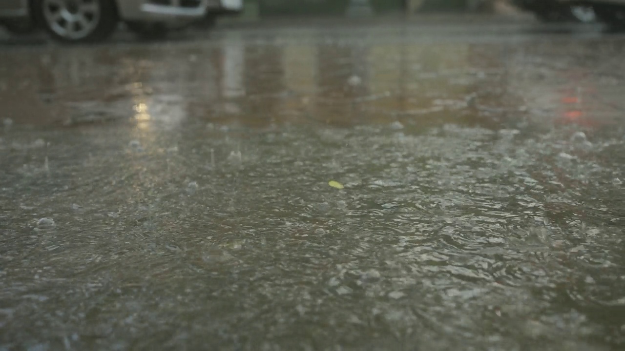 特写:雨滴落在人行道上的水坑里，汽车在背景中行驶。城里下起了暴雨。视频素材