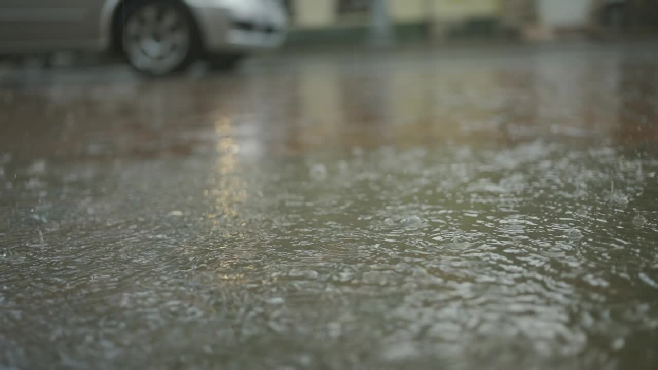 雨滴落在路上，背景是汽车行驶。城里下起了暴雨。视频素材