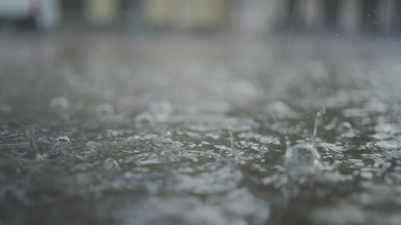 特写:雨滴落在人行道上的水坑里，汽车在背景中行驶。城里下起了暴雨。视频素材