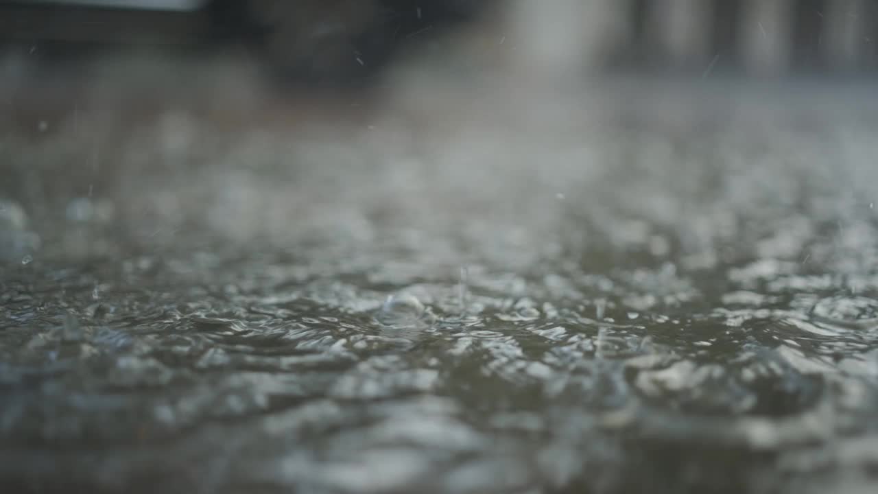 特写:雨滴落在人行道上的水坑里，汽车在背景中行驶。城里下起了暴雨。慢动作视频素材