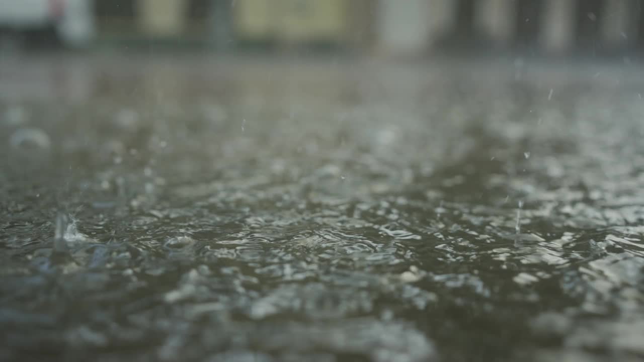 特写:雨滴落在人行道上的水坑里，汽车在背景中行驶。城里下起了暴雨。慢动作视频素材