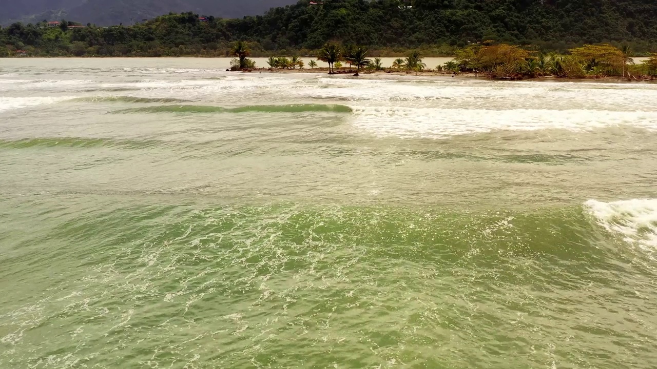 无人机随着海浪飞过海面，飞向长满棕榈树的海滩视频素材