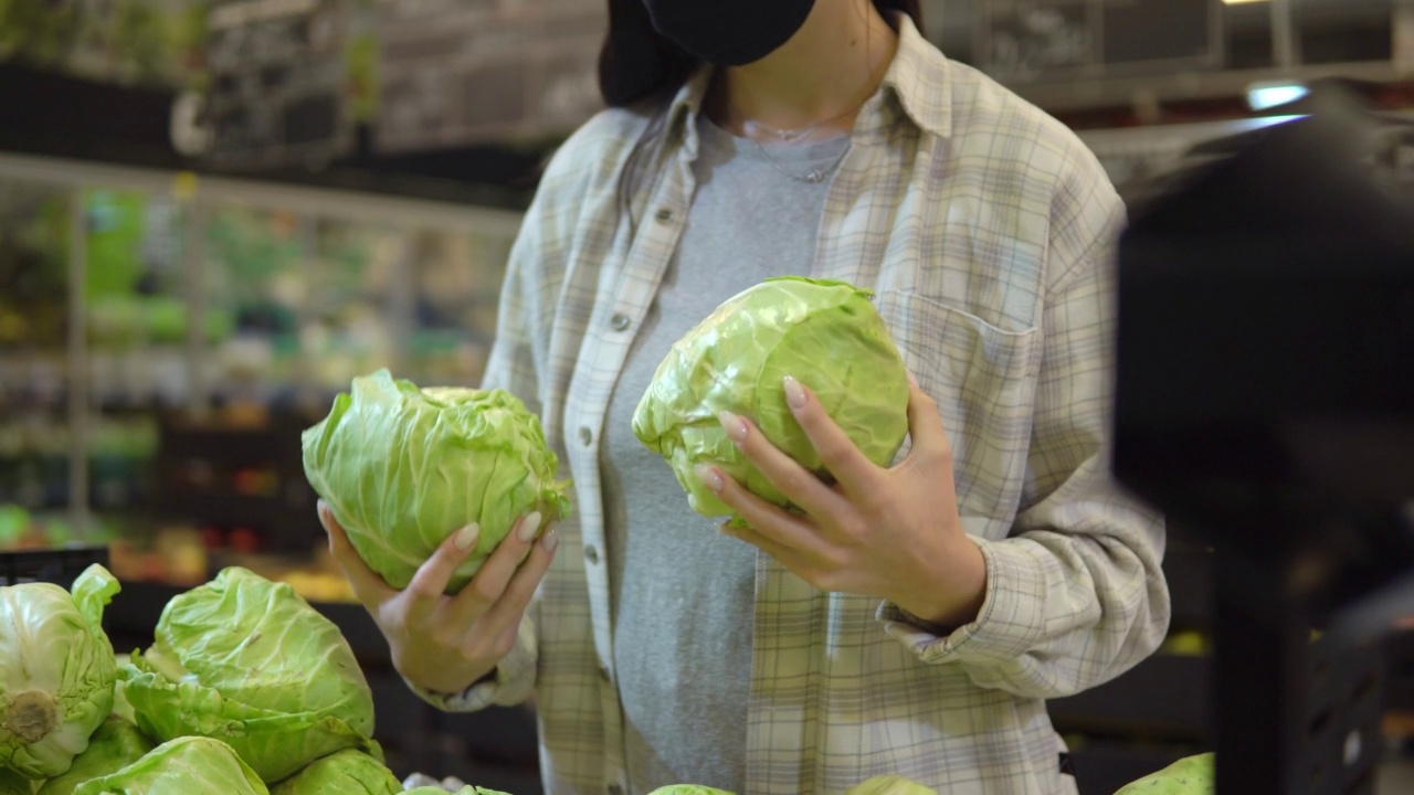 戴着防护口罩的年轻女子在超市挑选卷心菜视频素材