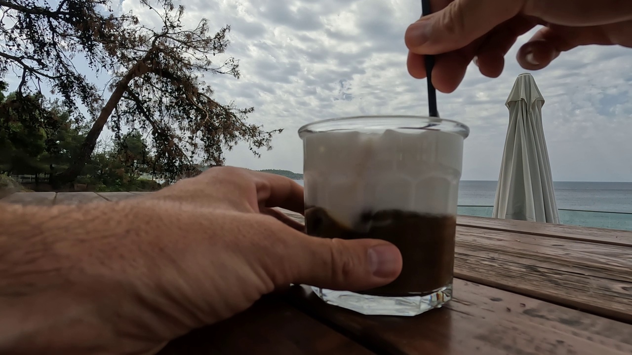 一个男人和弗雷多在海边酒吧喝卡布奇诺视频素材