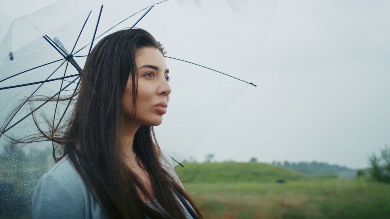 一个悲伤的亚美尼亚女人撑着伞在雨中行走。她喜欢这种天气。视频素材