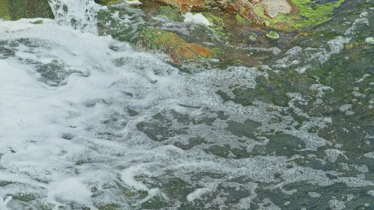 美丽的山间瀑布流过岩石，它的水冲刷着石头和树木视频素材