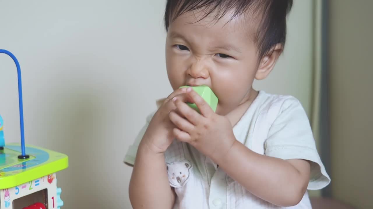 可爱的亚洲女婴开心地咬着长牙玩具，宝宝开始长牙发育视频下载