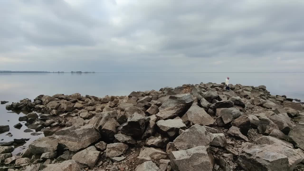 早春。景观。一个十几岁的女孩沿着河或海附近的岩石海岸散步。视频素材