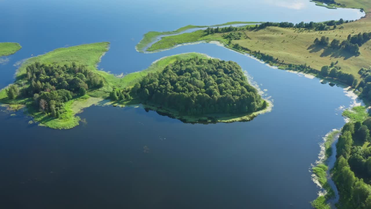 从上面俯瞰美丽的湖陆地，风景如画的岛屿覆盖着绿色的树木和草地。空中，飞行在蓝色的水面上，阳光反射在水中，就像夏日的镜子视频素材