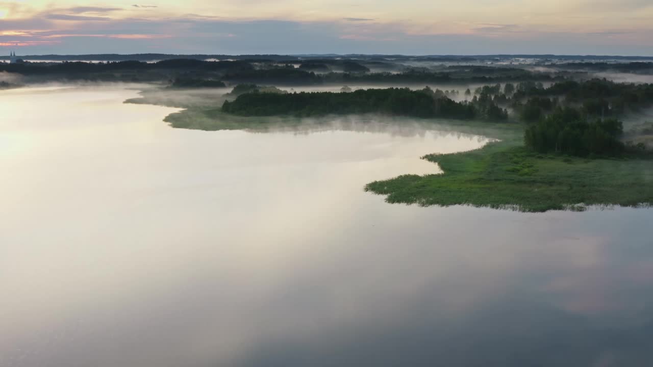 黎明前空中有雾的早晨。无人机在水面和湖岸上空飞行。在地面上移动的雾云地平线上的针叶林和草地。日出时田园诗般的景色视频素材