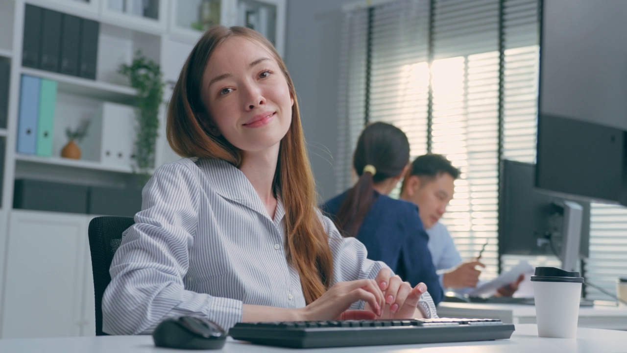 白人女商人在办公室打字的肖像。迷人的年轻女孩员工穿着正装坐在桌子上，使用电脑计划工作项目在公司的工作场所。视频素材