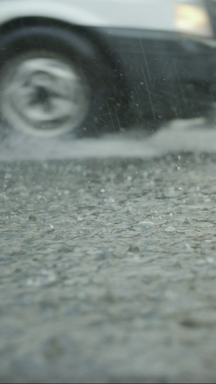 垂直视频:雨滴落在路上的特写，汽车在背景中行驶。城里下起了暴雨。视频素材