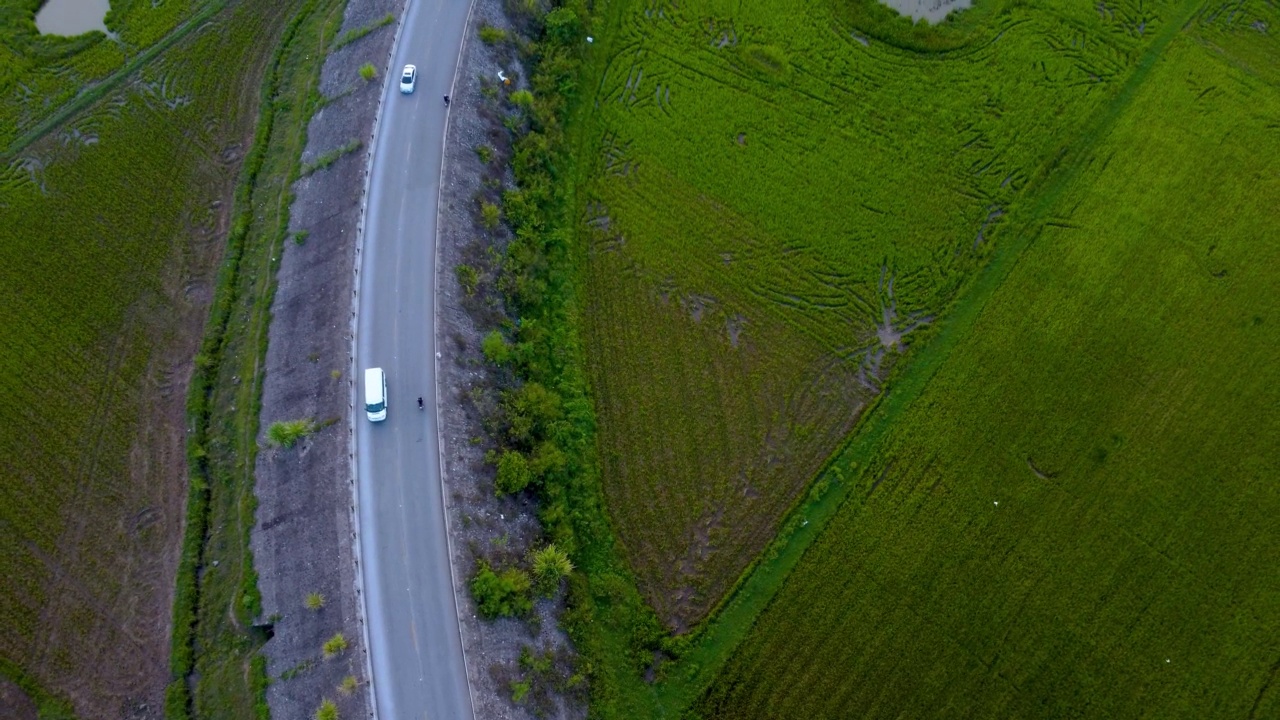 鸟瞰乡村公路，汽车穿梭在绿色的农田之间视频素材