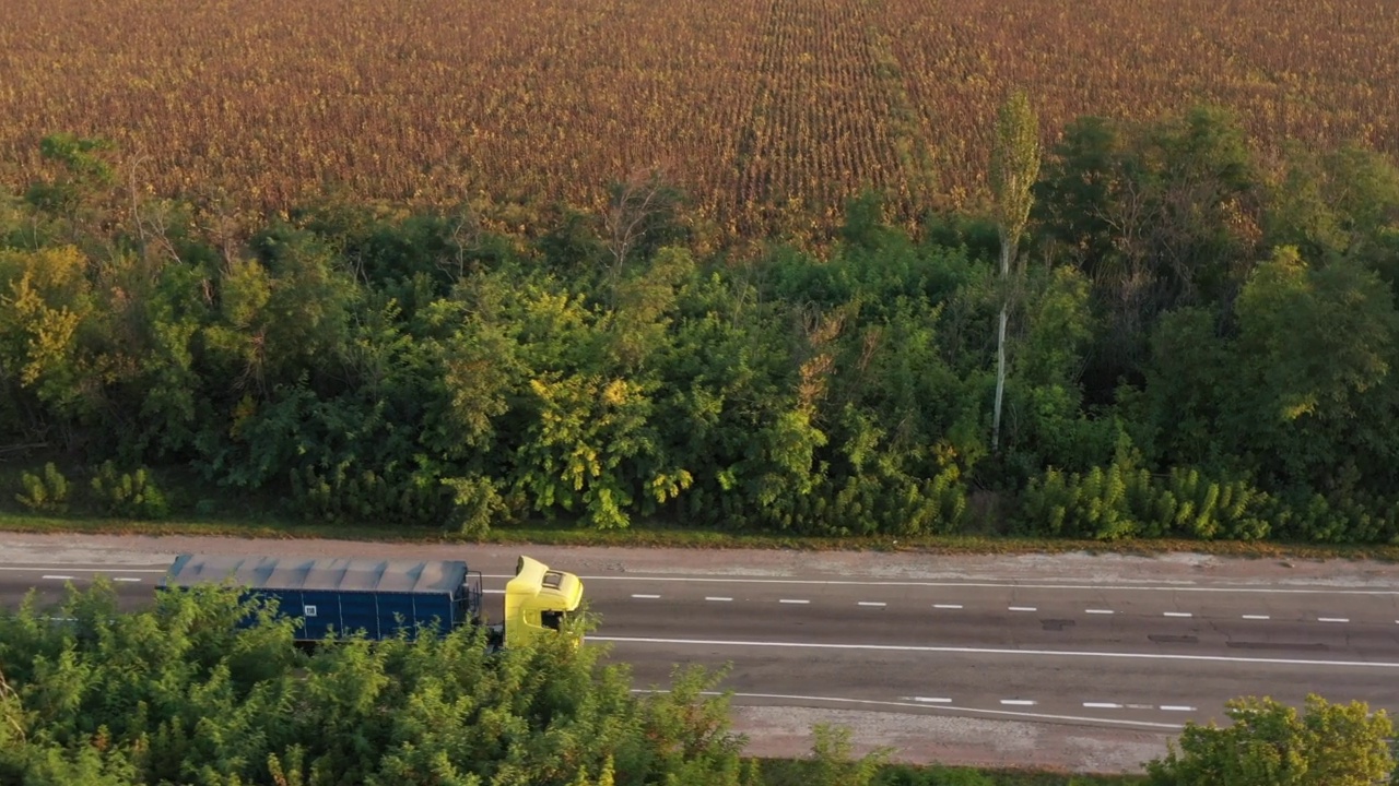 航拍的一辆谷物卡车在夏日夕阳下行驶在美丽的乡村道路上。无人机拍摄的卡车行驶在乡间的高速公路上，沿途有农田和树木。视频素材