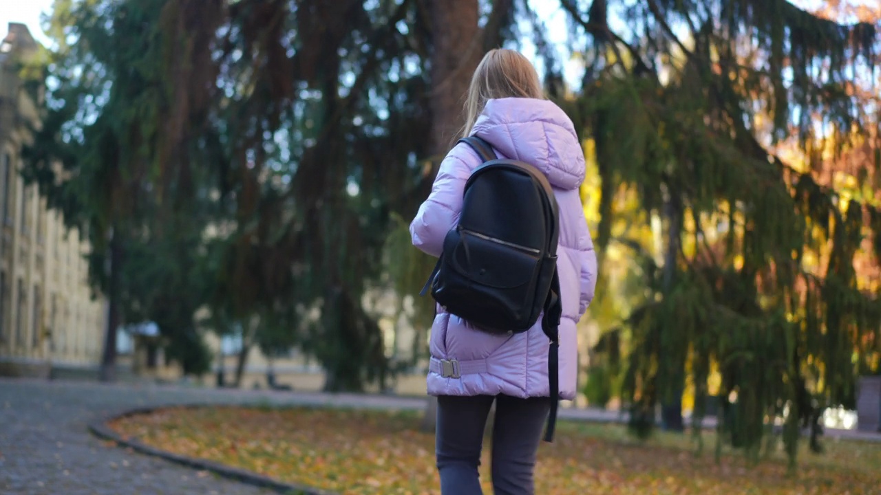 自信聪明的少女背着双肩包走向大学。漂亮的白人女学生在秋日背着背包在户外散步的肖像。视频素材