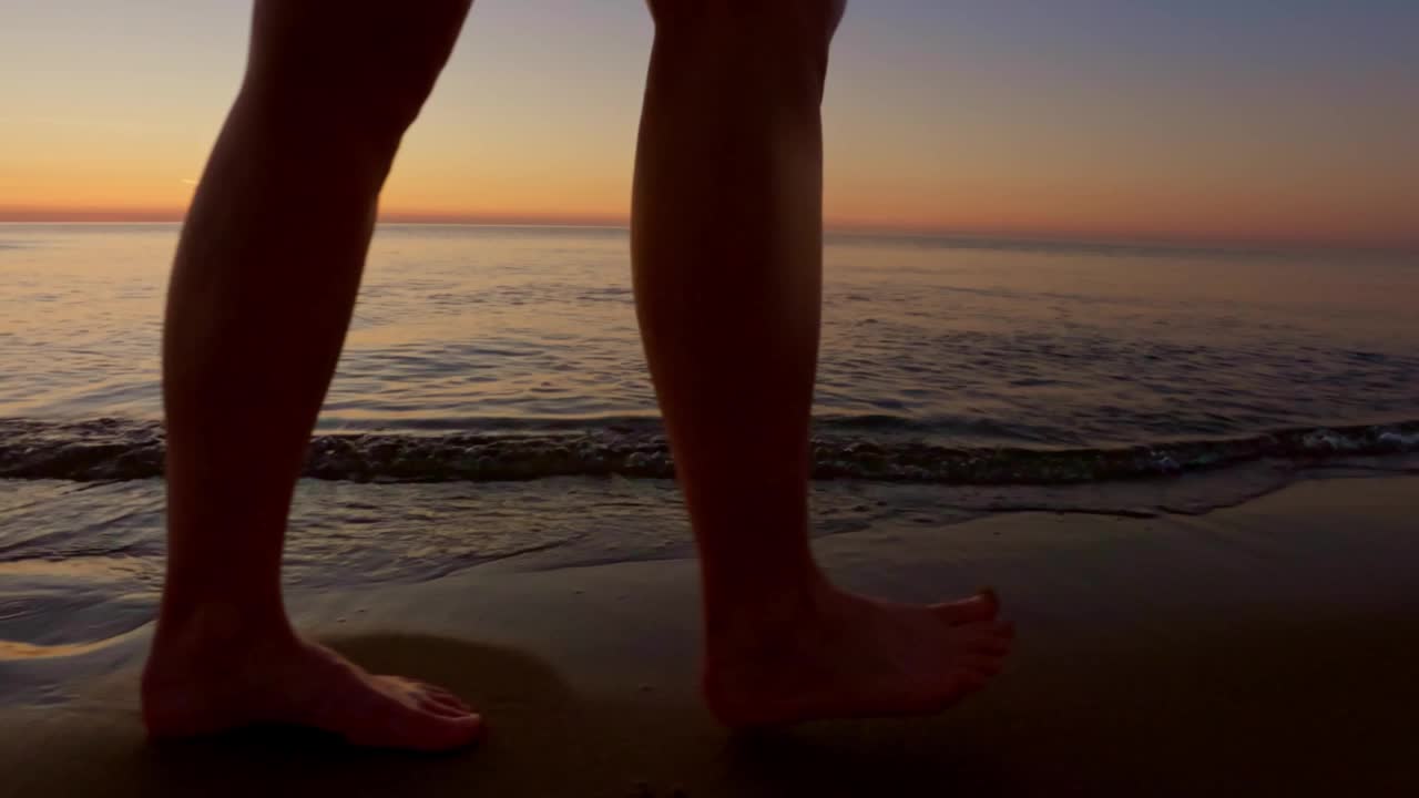 在一个平静温暖的夏夜，一个人光着脚走在海边。视频下载