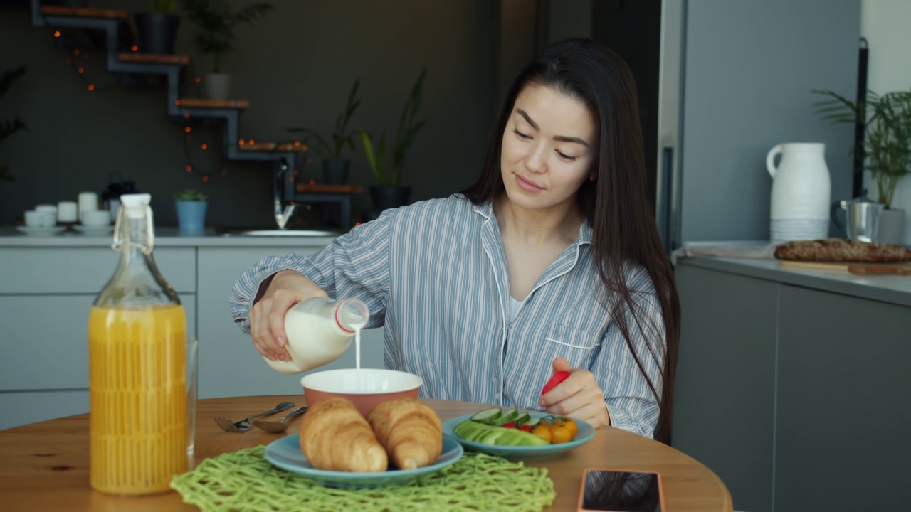 亚洲妇女倒牛奶在碗在家里厨房早餐慢动作视频素材