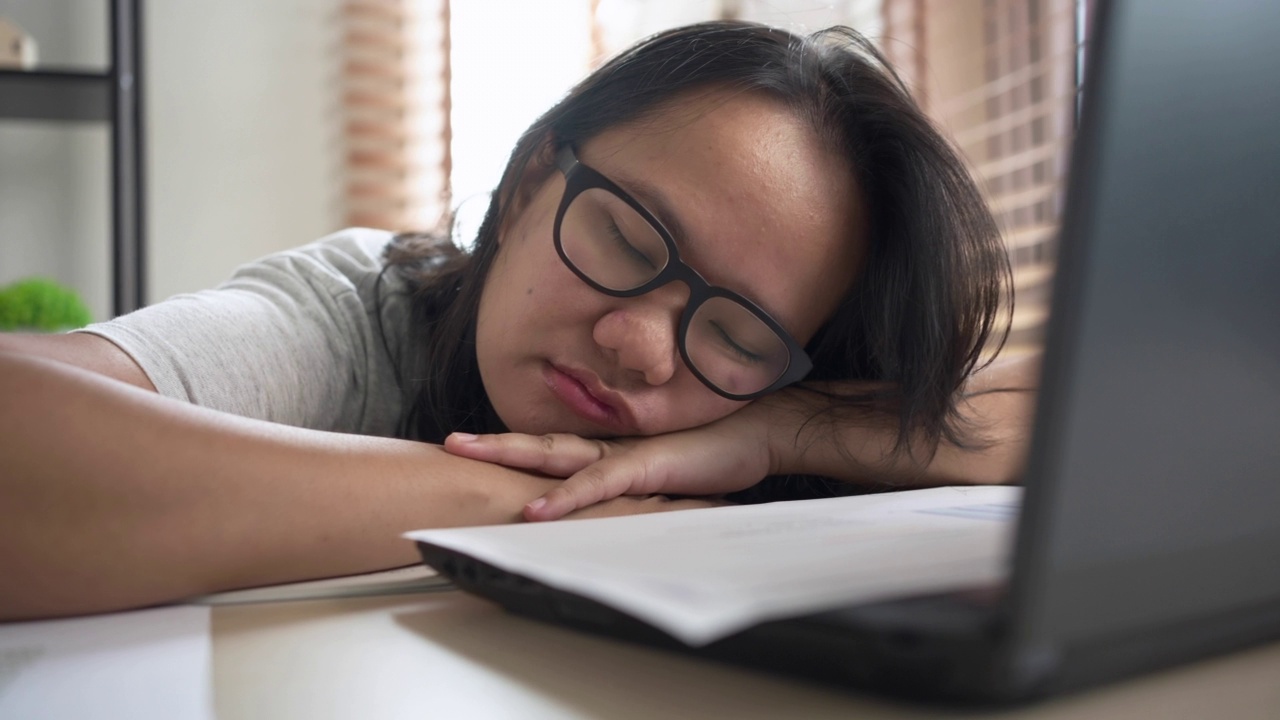 试过一位亚洲女性在家用笔记本电脑工作时睡在桌子上。在自由职业中工作到最后期限视频素材