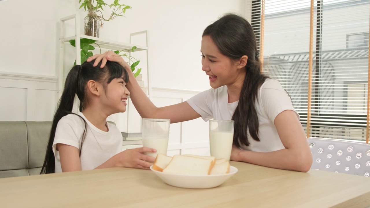 健康的亚洲妈妈和女儿一起在餐桌上喝鲜奶。视频素材