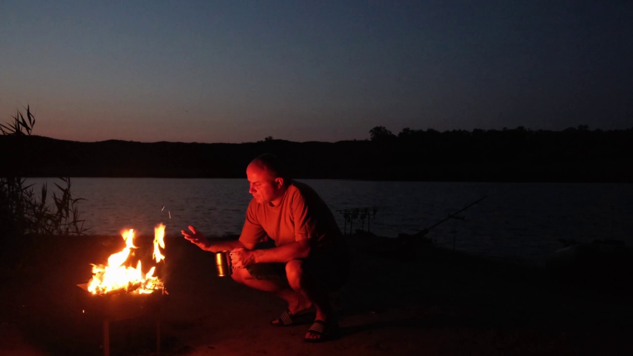 一个人坐在河边的营火旁。夏夜钓鱼之旅视频素材