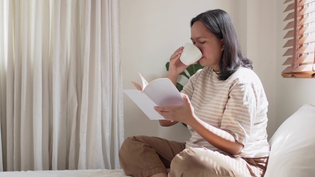 快乐的女人早上在家里看书喝咖啡或茶。周末在家看一本喜欢的书放松视频素材